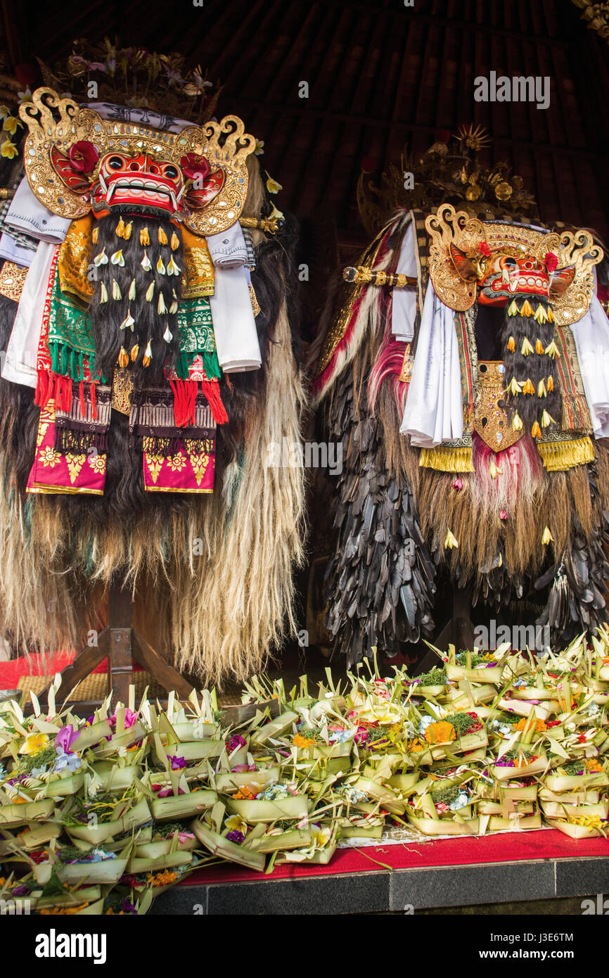 Due colorati e allestita Barong costumi della mitologia Balinese, folklore e leggenda con pile di offerte ai loro piedi alla cerimonia di Bali Foto Stock
