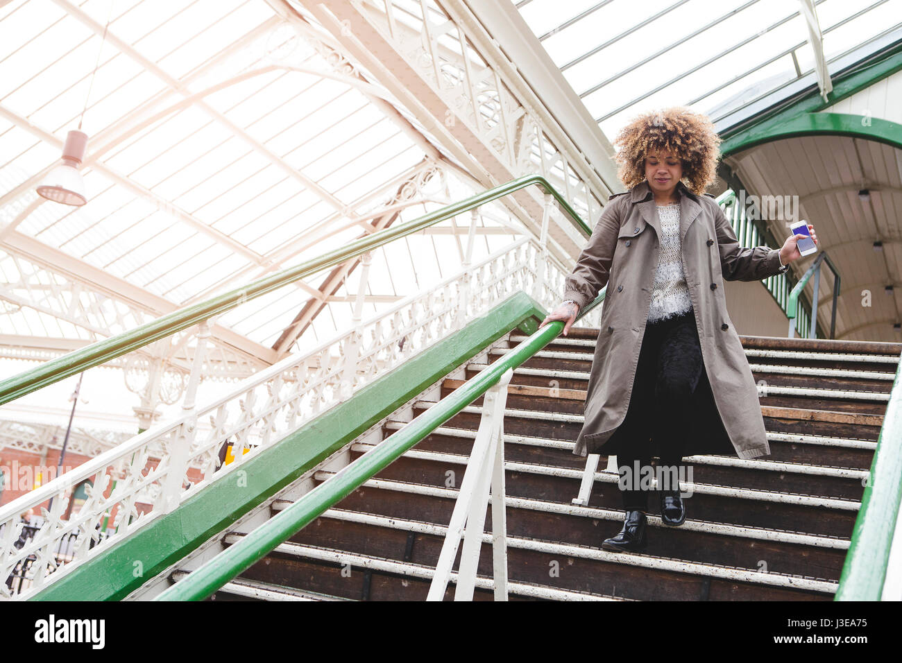 Donna in corsa giù per le scale in corrispondenza di una stazione ferroviaria con il telefono in mano. Ella è in ritardo per il treno. Foto Stock