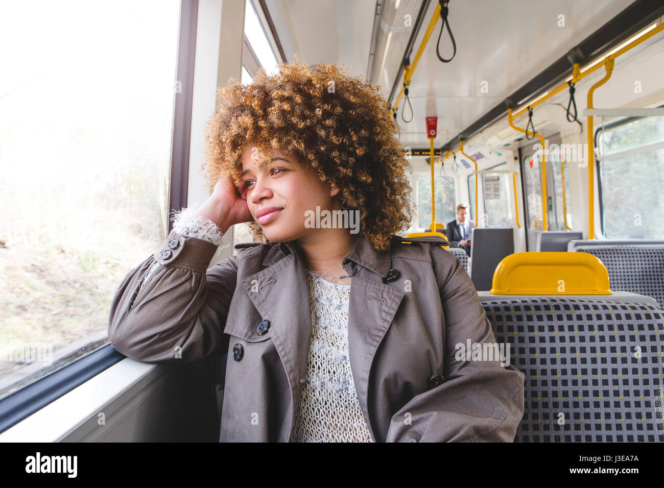 Donna seduta su un treno. Ella ha il suo gomito sul davanzale della finestra e poggia la sua testa sulla sua mano, guardando fuori dalla finestra. Foto Stock
