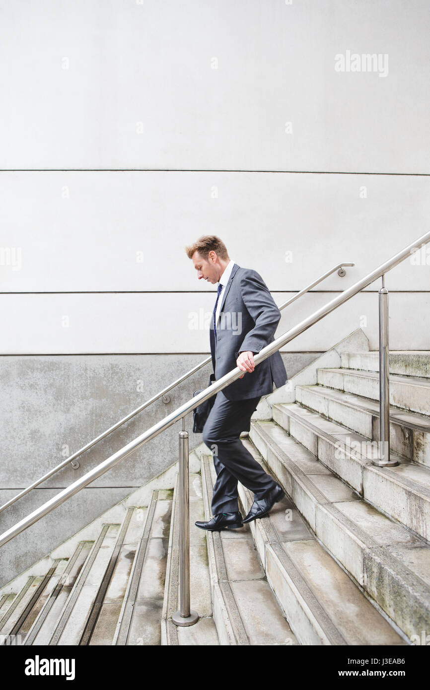 Imprenditore per il suo modo di lavorare. Egli è vestito con un abito formale e scendendo alcuni gradini. Foto Stock