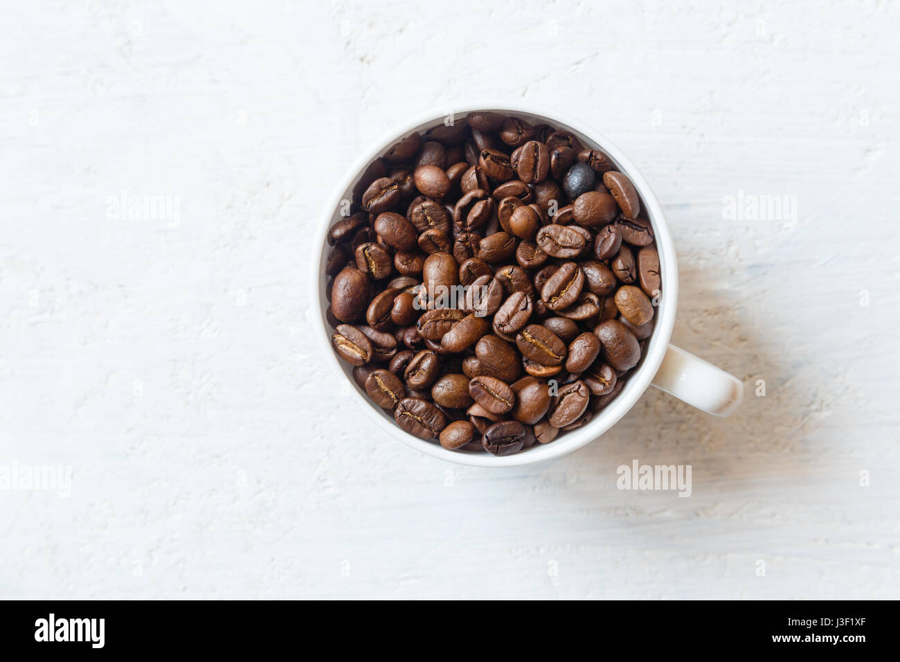 Tazza da caffè piena di chicchi di caffè in bianco sullo sfondo di legno Foto Stock