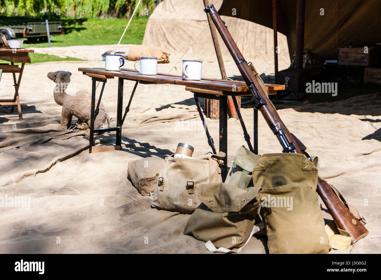 1940s ricreazione evento. Ratti nel deserto vita Storia Gruppo, tavolo con un fucile sostennero contro e tre tazze di tè. Foto Stock