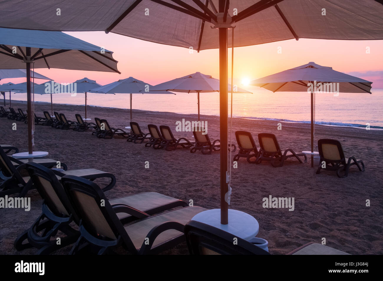 Fila di ombrelloni sulla spiaggia del mare. Vista tranquilla del mare Mediterraneo. Incredibile rosa alba con cielo chiaro. Location posizione: Turchia Kemer. Foto Stock