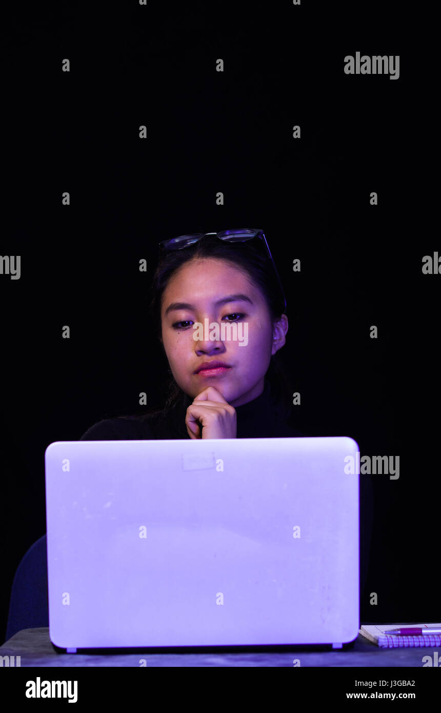 Ritratto di una bellissima e Smart girl hacker con il computer portatile su sfondo scuro utilizzando bicchieri nella sua testa mentre lei sta lavorando Foto Stock