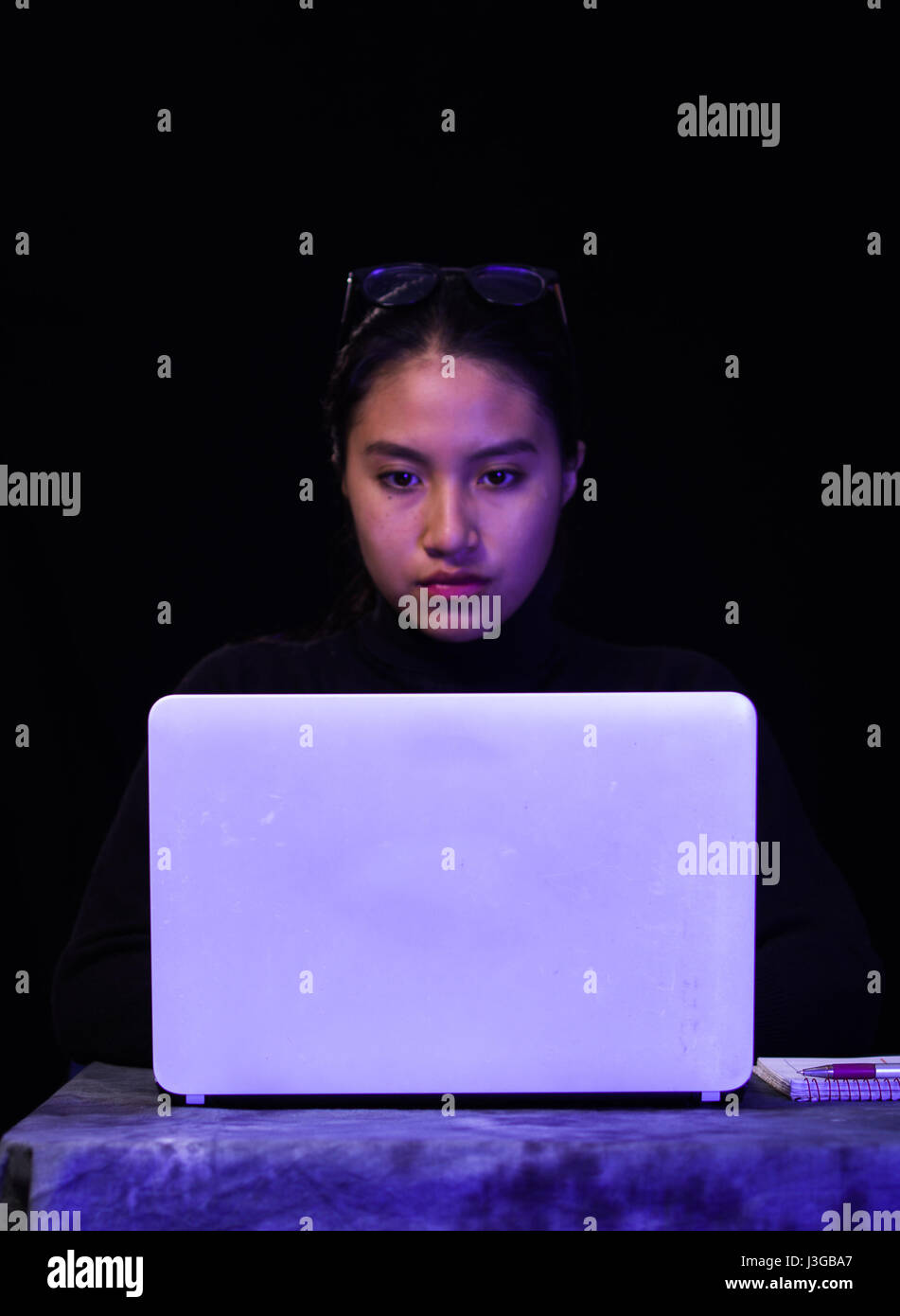 Ritratto di una bellissima e Smart girl hacker con il computer portatile su sfondo scuro con l'utilizzo di bicchieri nella sua testa Foto Stock
