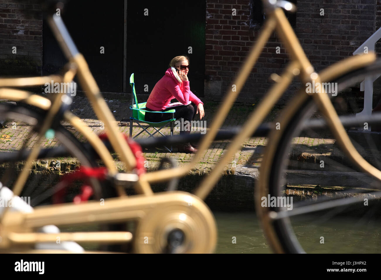 L'Europa, Paesi Bassi Utrecht, giovane donna seduta al sole in città canal Oudegracht ed effettua una chiamata telefonica. Foto Stock