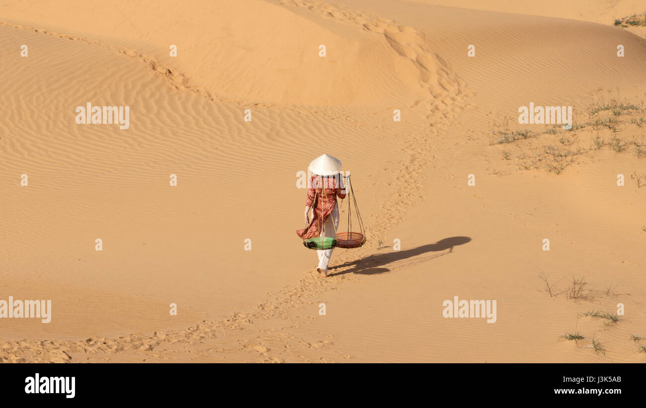 Donna asiatica che trasportano due cestelli attaccato ad un bastone di legno sulle sue spalle nel deserto a mezzogiorno e andare a casa. Foto Stock