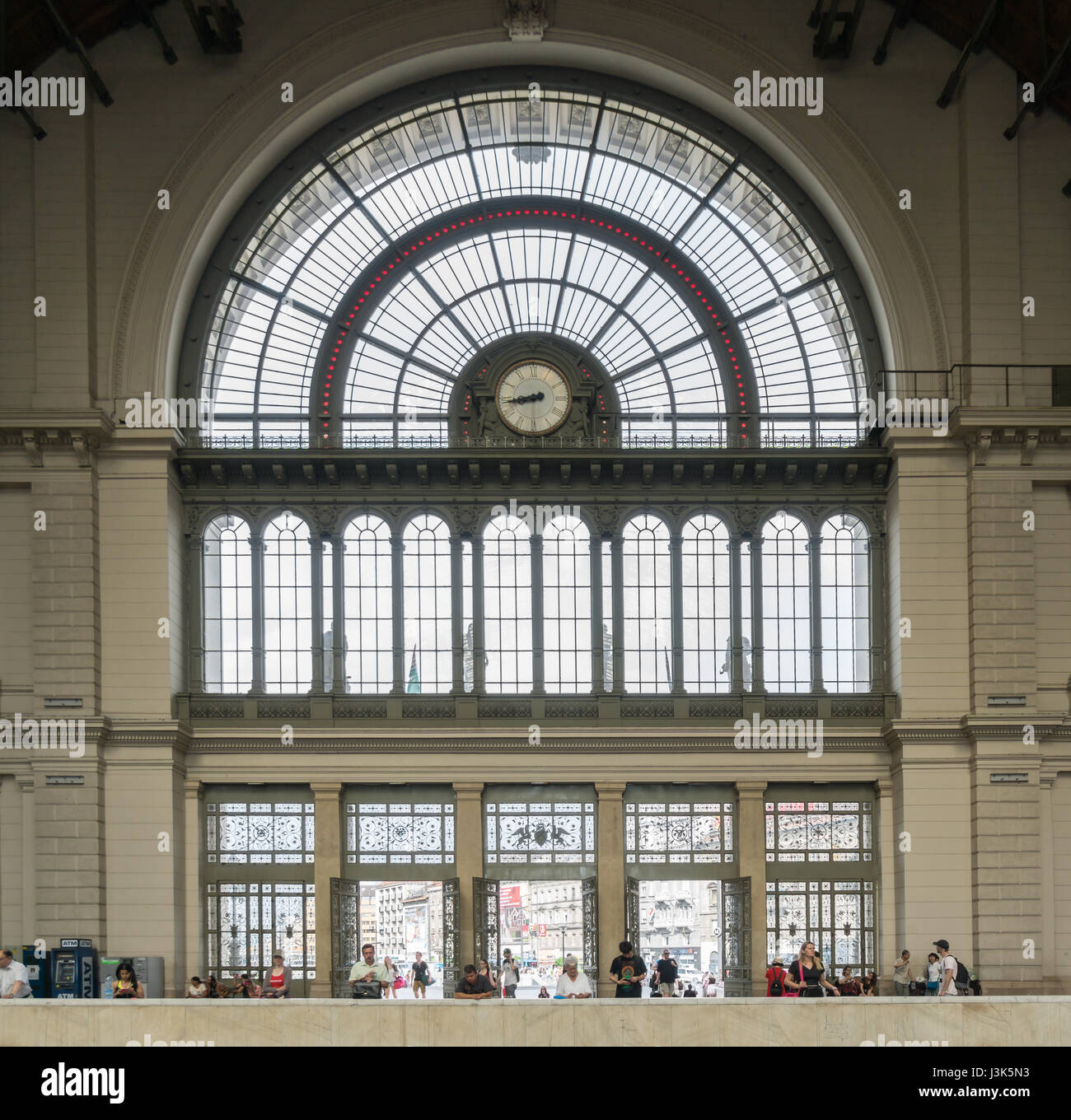 Molte persone attendere all'interno delle porte anteriori di Budapest alla Stazione ferroviaria di Keleti, di fronte alla grande finestre decorative. Foto Stock