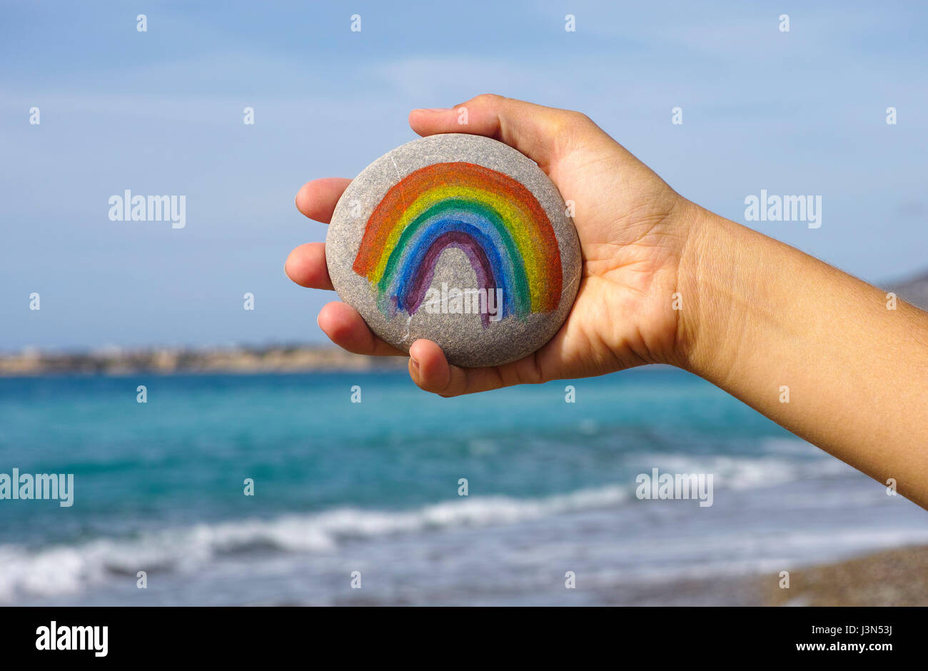 Donna tenere in mano con ciottoli rainbow dipinte contro il blu del cielo e del mare. Foto Stock