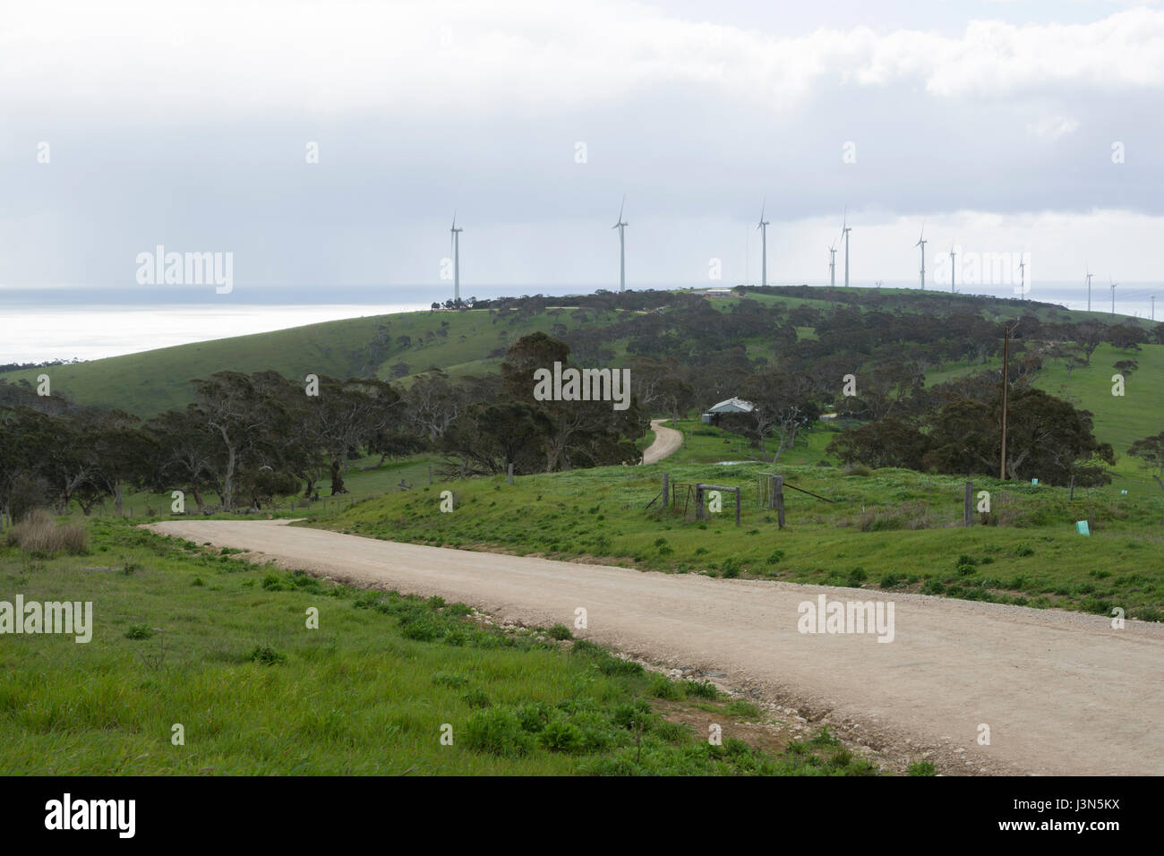 South Australian Bush su strada sterrata con turbine eoliche alacremente la generazione di elettricità sulle colline e con vista oceano in background. Penisola di Fleurieu, essere Foto Stock