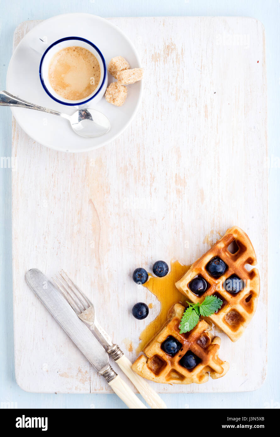 Tazza di caffè, morbide cialde belghe con mirtilli freschi e marple sciroppo sul dipinto di bianco di tavola di legno su fondo azzurro Foto Stock