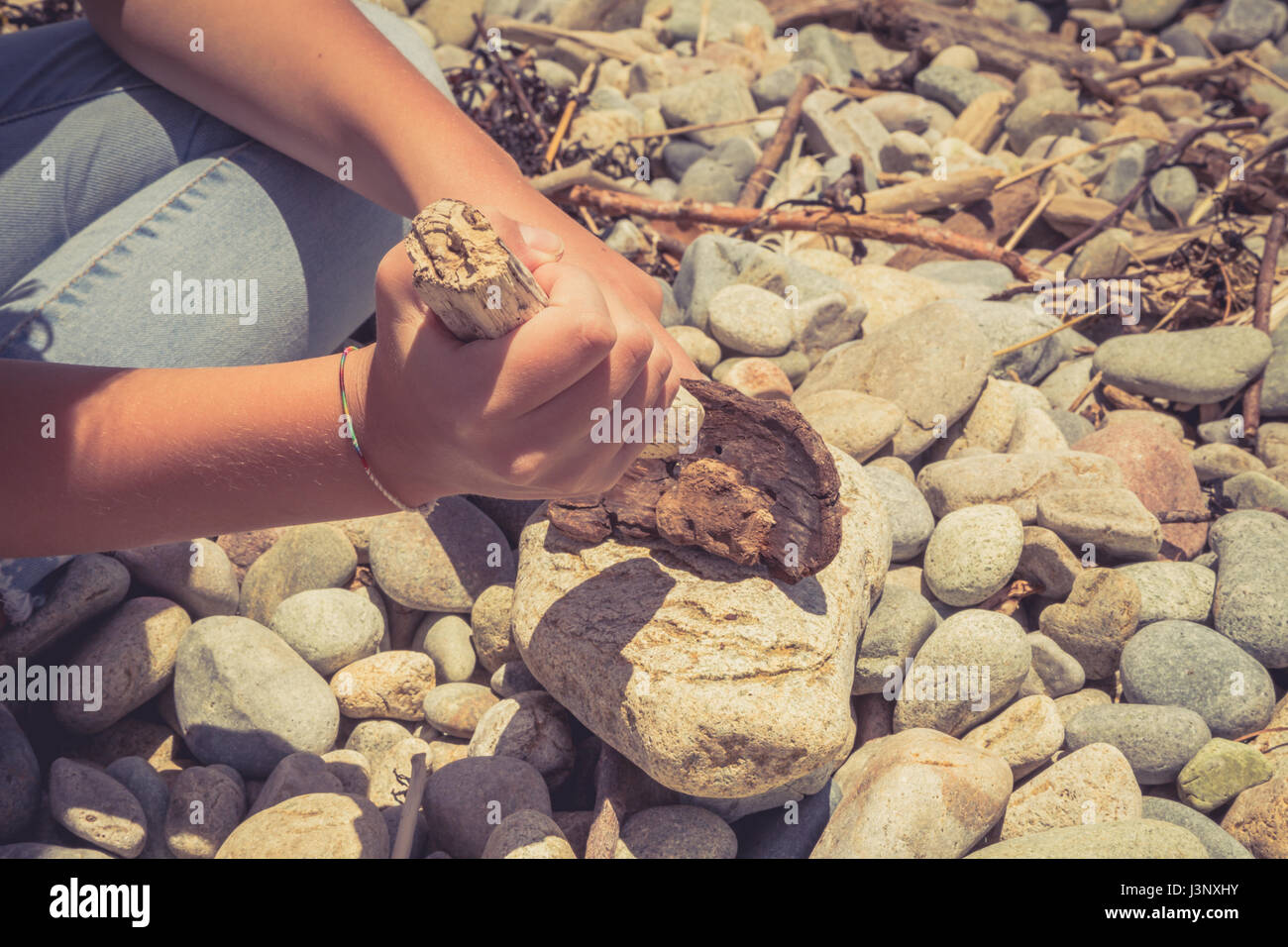 Le mani di una giovane ragazza con dei pezzi di legno e messa a fuoco sulla spiaggia con le pietre levigate. Foto Stock
