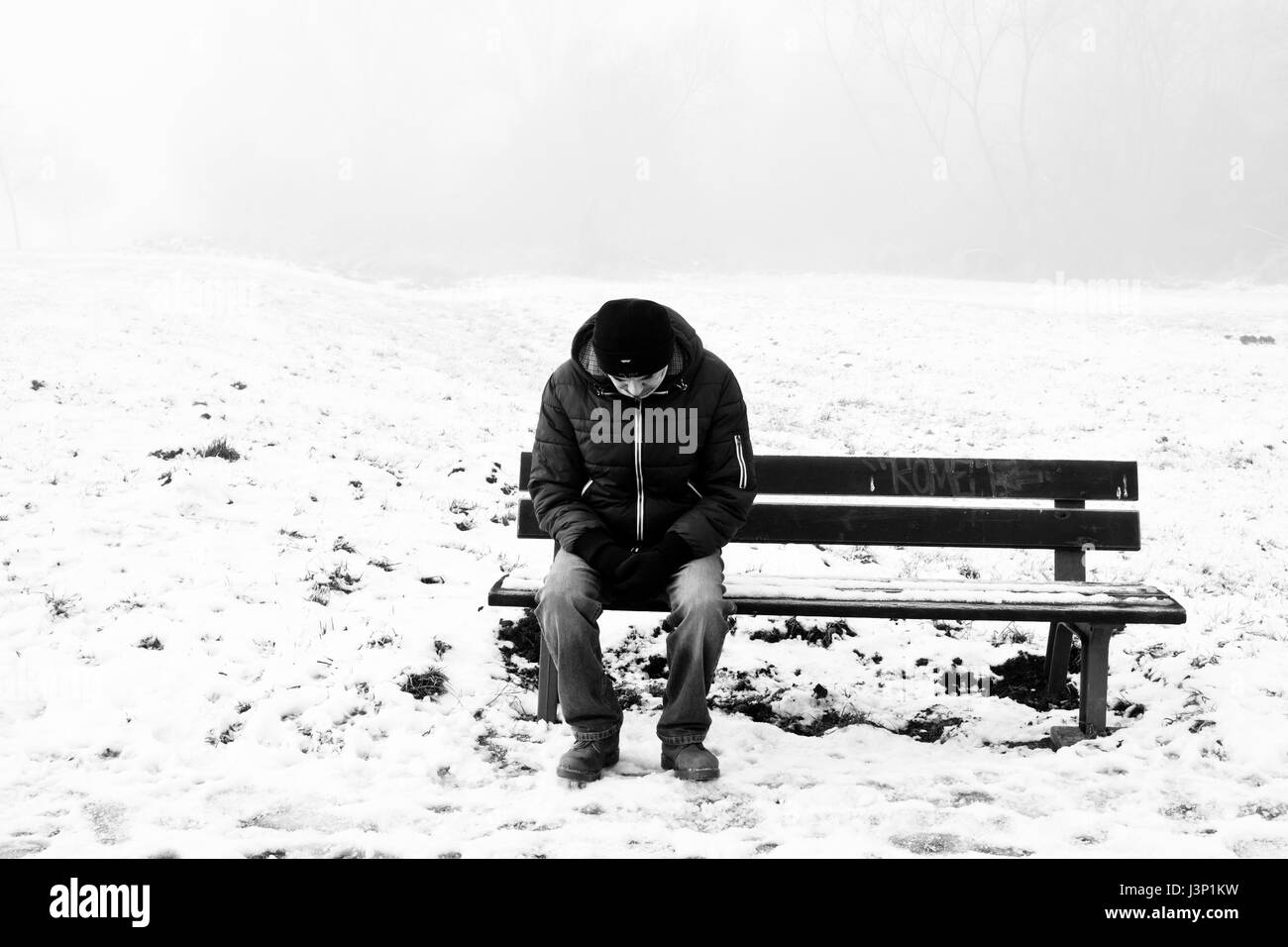 Uomo seduto su una panchina, soli e tristi, in un freddo inverno snow day Foto Stock
