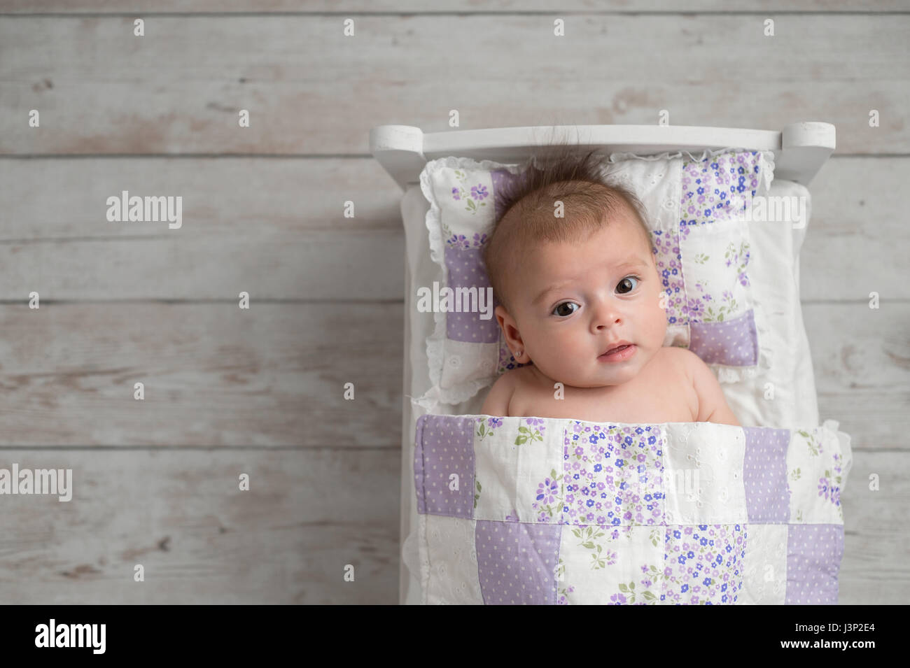 Un overhead shot di quattro mesi di età, avviso, bambina. Ella è giacente in un piccolo letto e guardando verso l'alto la fotocamera. Foto Stock