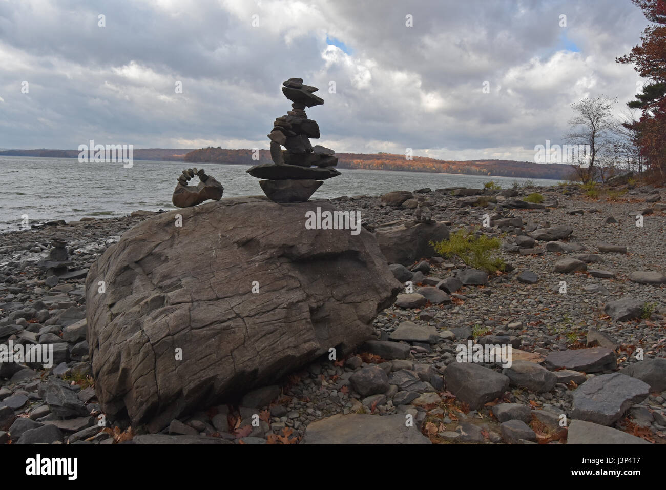 Le sculture in pietra sulla spiaggia rocciosa con moody cielo sopra il lago luminoso Foto Stock