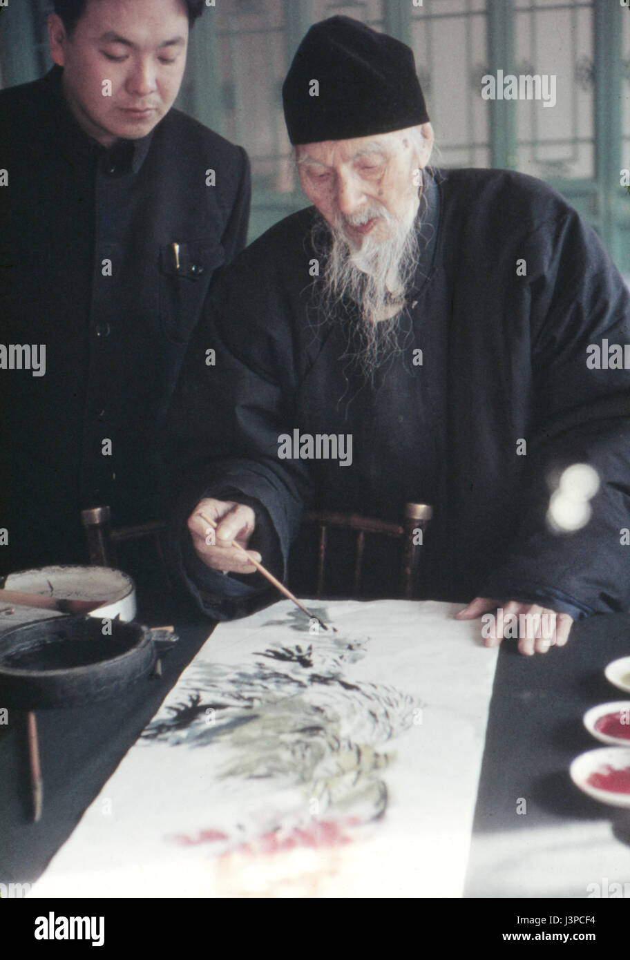 Qi Baishi pittura a scorrere nel suo studio a Pechino nel 1957, mesi prima di morire. Guardando sopra la sua spalla è suo figlio. Foto Stock