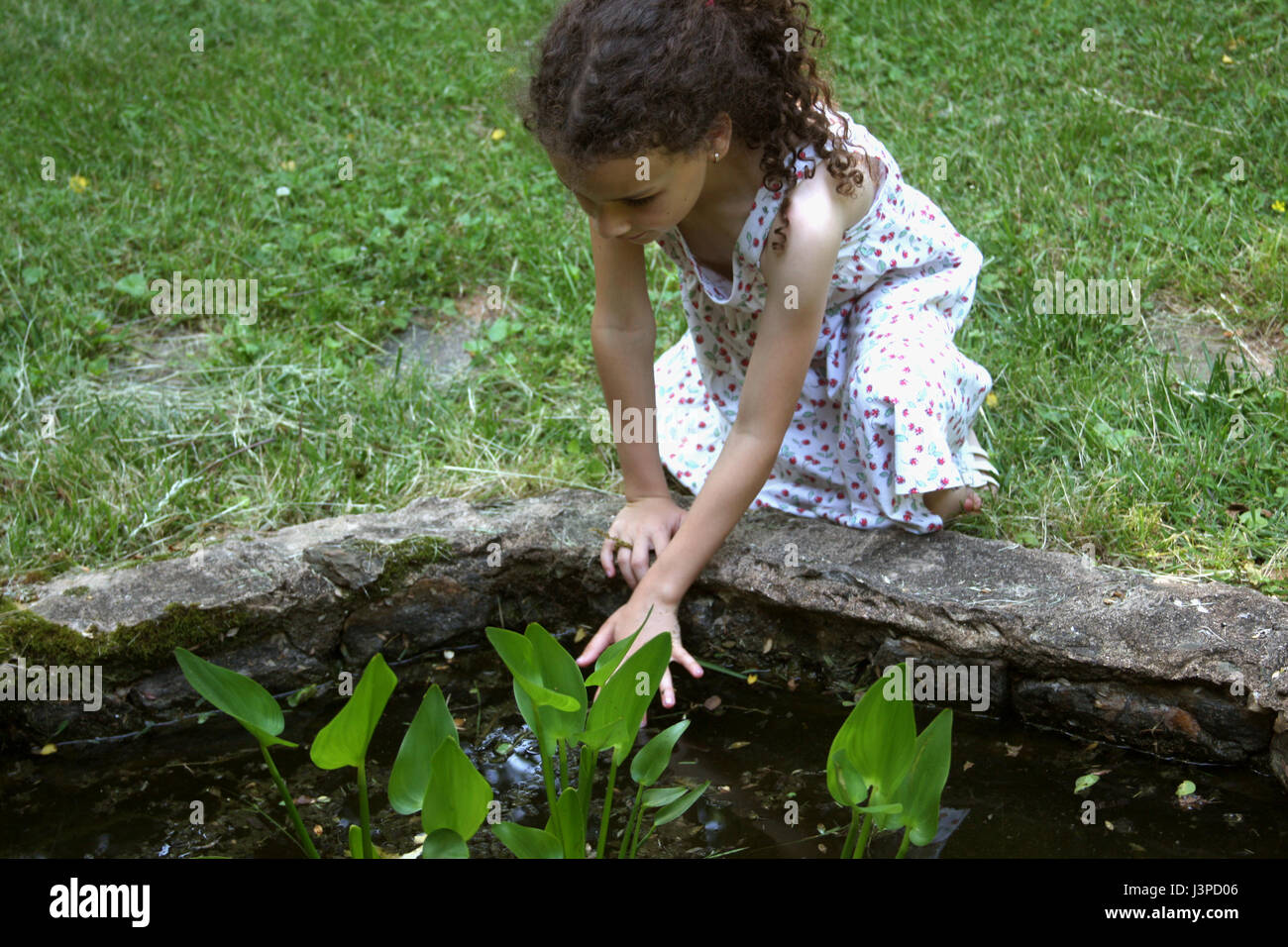 Ragazza giovane toccando acqua in stagni artificiali Foto Stock