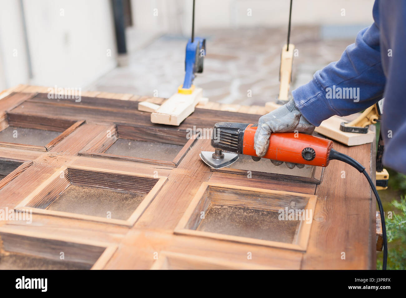 Carpenter al lavoro con la smerigliatrice angolare. La manutenzione e il restauro di una vecchia porta di legno. Foto Stock