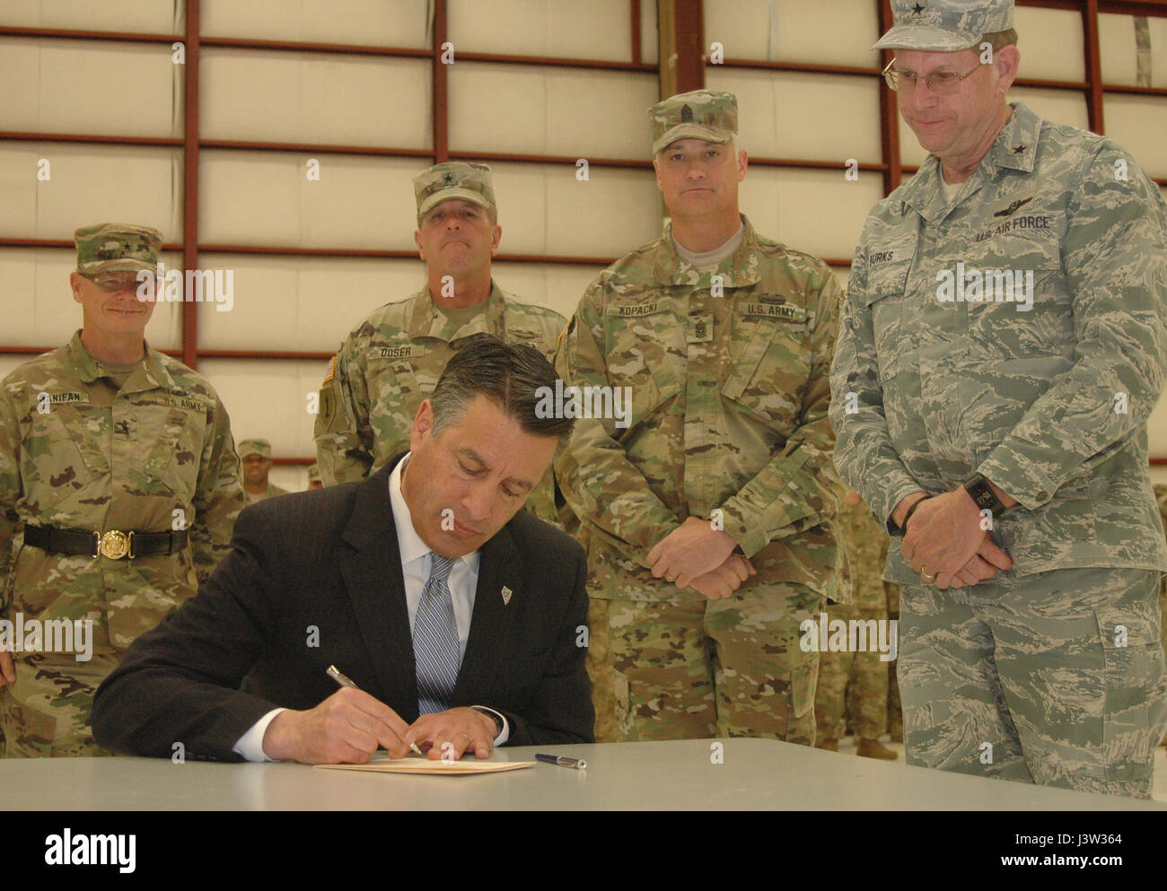 Nevada Gov. Brian Sandoval, seduto, emana un pro-Nevada Guard bill in legge mentre Nevada leadership di guardia funzionari guardare a conclusione di un Welcome Home Cerimonia per circa 180 Nevada guardia esercito di soldati di segnale il 9 aprile a Reno, Nev. Foto Stock