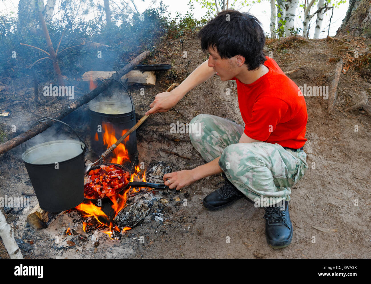 Un adolescente cucina su un fuoco aperto in una spedizione Foto Stock