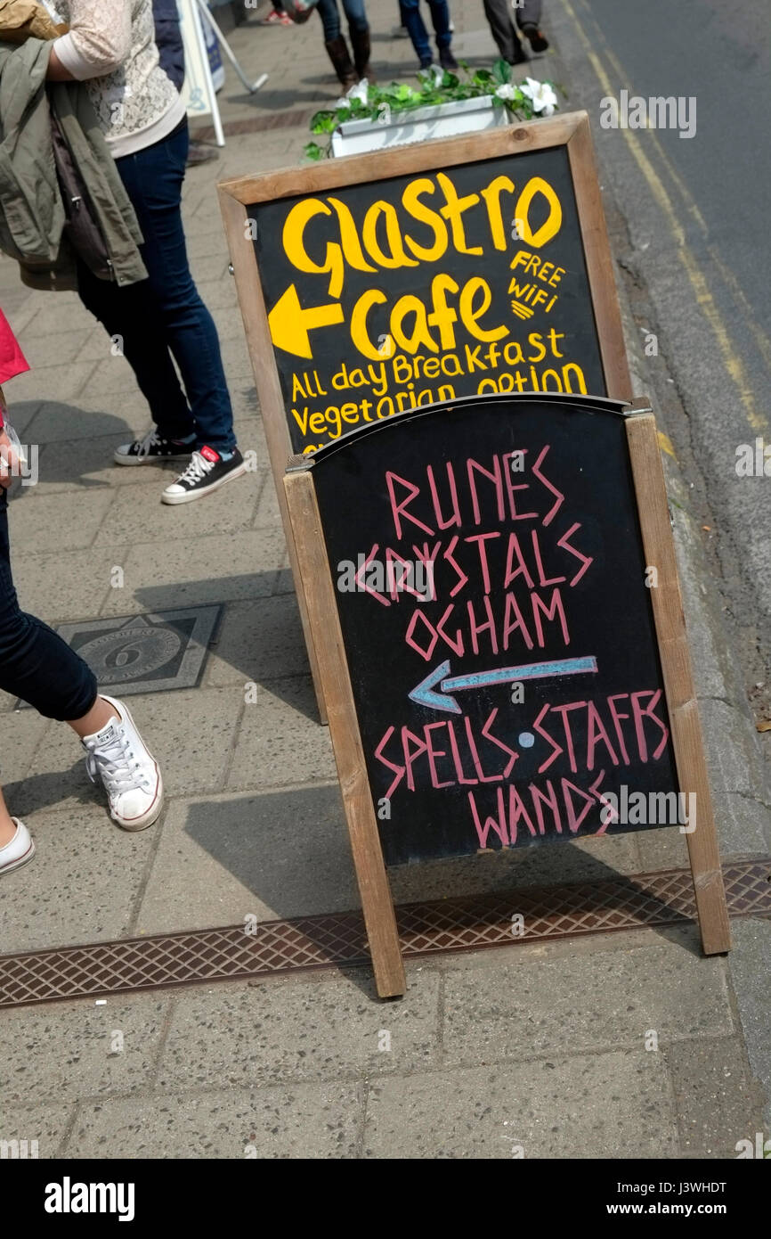 High street cartelli pubblicitari per un cafe e un negozio di rune, cristalli, ogham, incantesimi, wands e bastoni, a Glastonbury, Somerset, Regno Unito Foto Stock