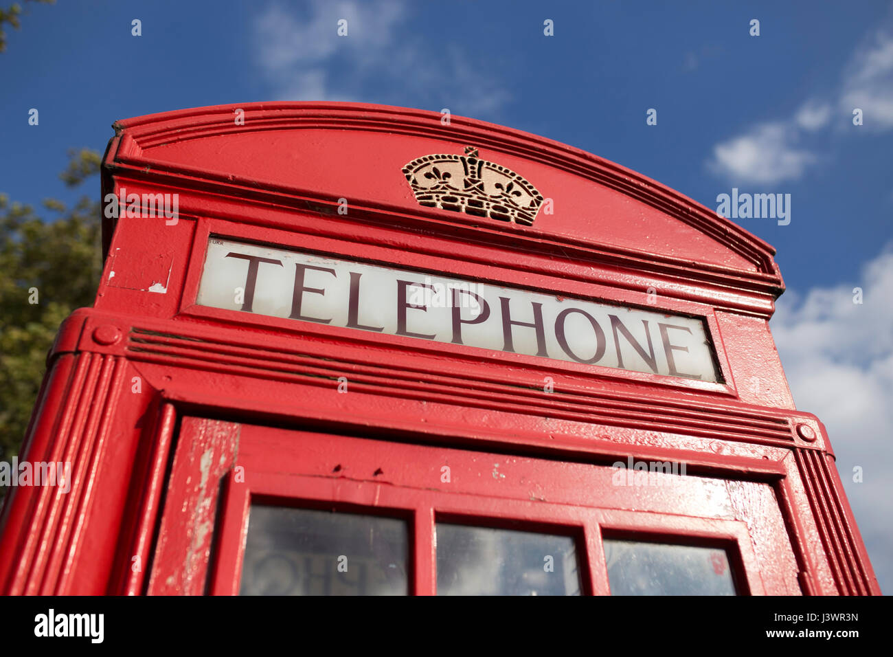Parte superiore del tradizionale telefono rosso casella nella parte anteriore del cielo blu e alberi. Foto Stock