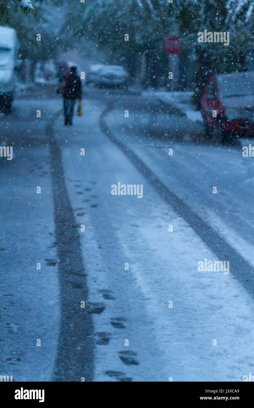Uomo che cammina tra le tracce di ruote di automobili in tempesta di neve in aprile. Il riscaldamento globale effetto. Foto Stock