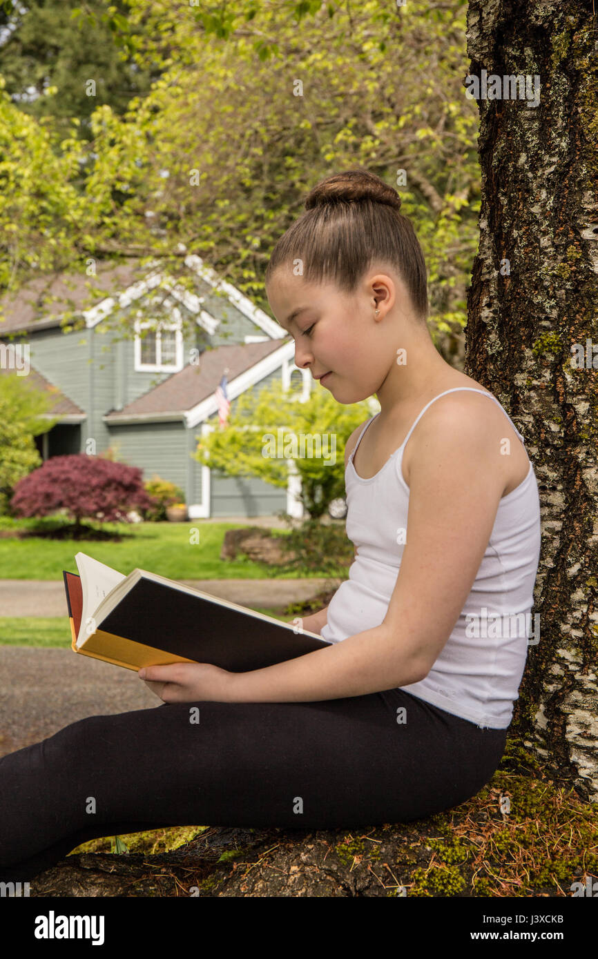 Di undici anni ragazza leggendo un libro all'ombra di un albero in Issaquah, Washington, Stati Uniti d'America Foto Stock