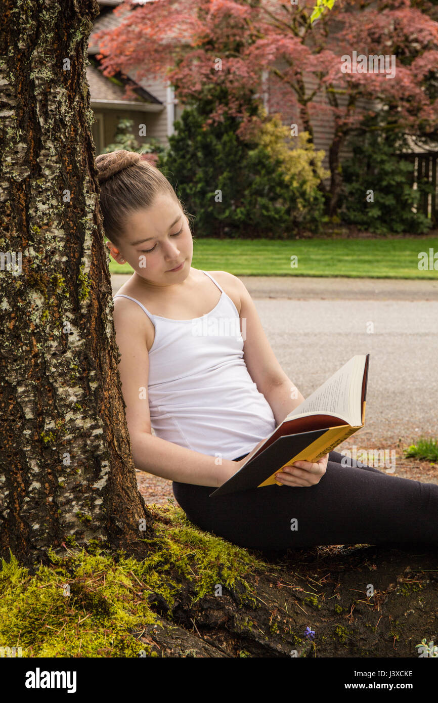 Di undici anni ragazza leggendo un libro all'ombra di un albero in Issaquah, Washington, Stati Uniti d'America Foto Stock