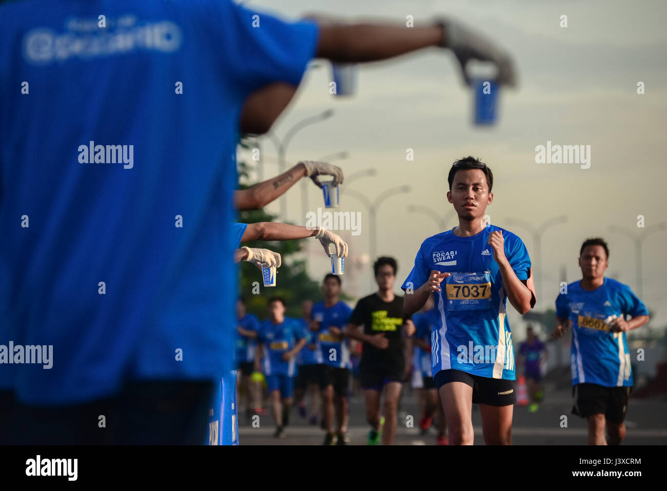 I corridori passano davanti a una stazione di bevande rinfrescanti mentre corrono nella corsa 'Pocari Sweat Run Indonesia 2015' a Tangerang, Indonesia. Foto Stock
