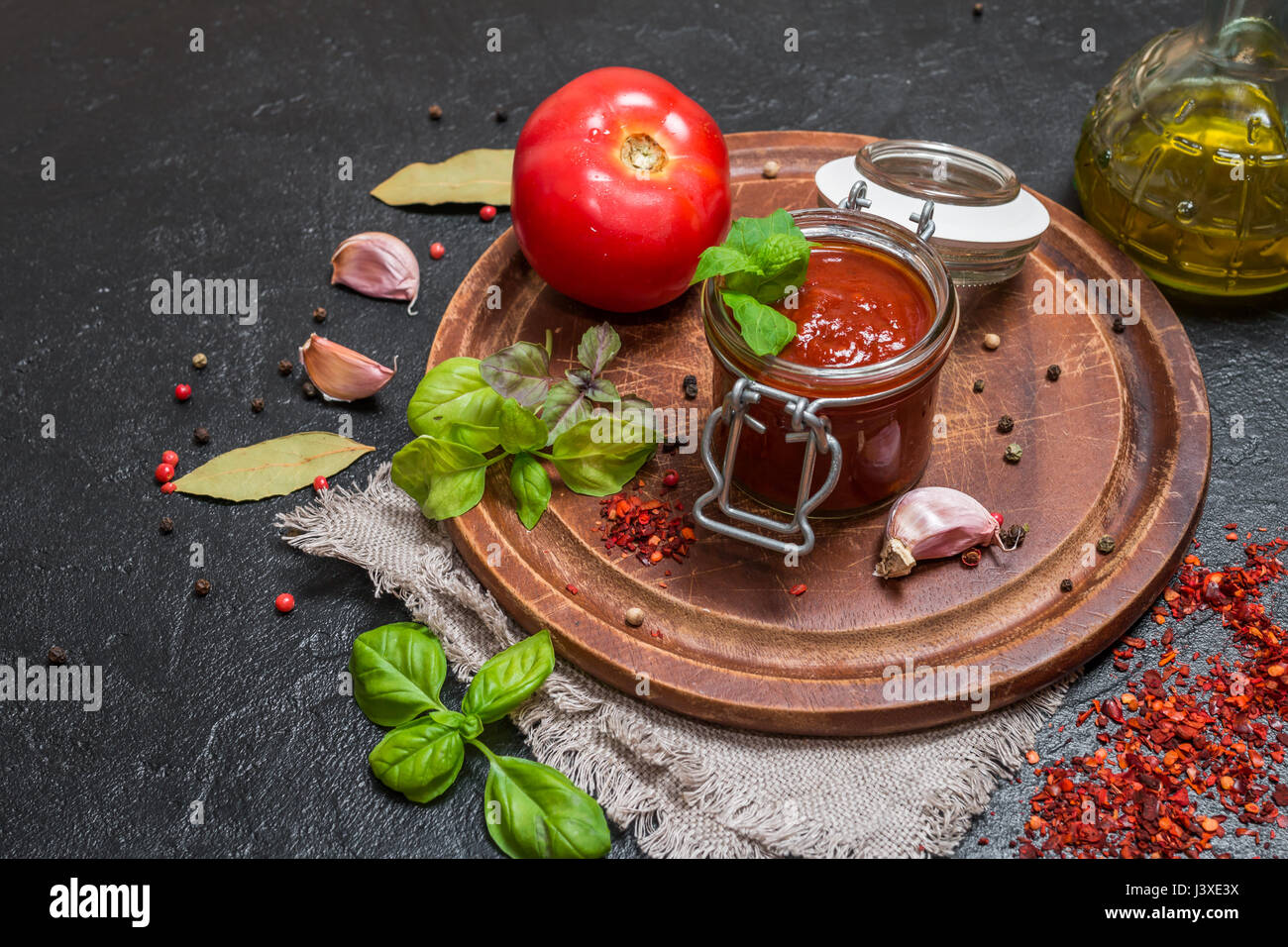 Il vasetto di vetro con fatti in casa classico pomodoro piccante pasta o pizza sauce. Italiano cibo sano su sfondo nero. Foto Stock
