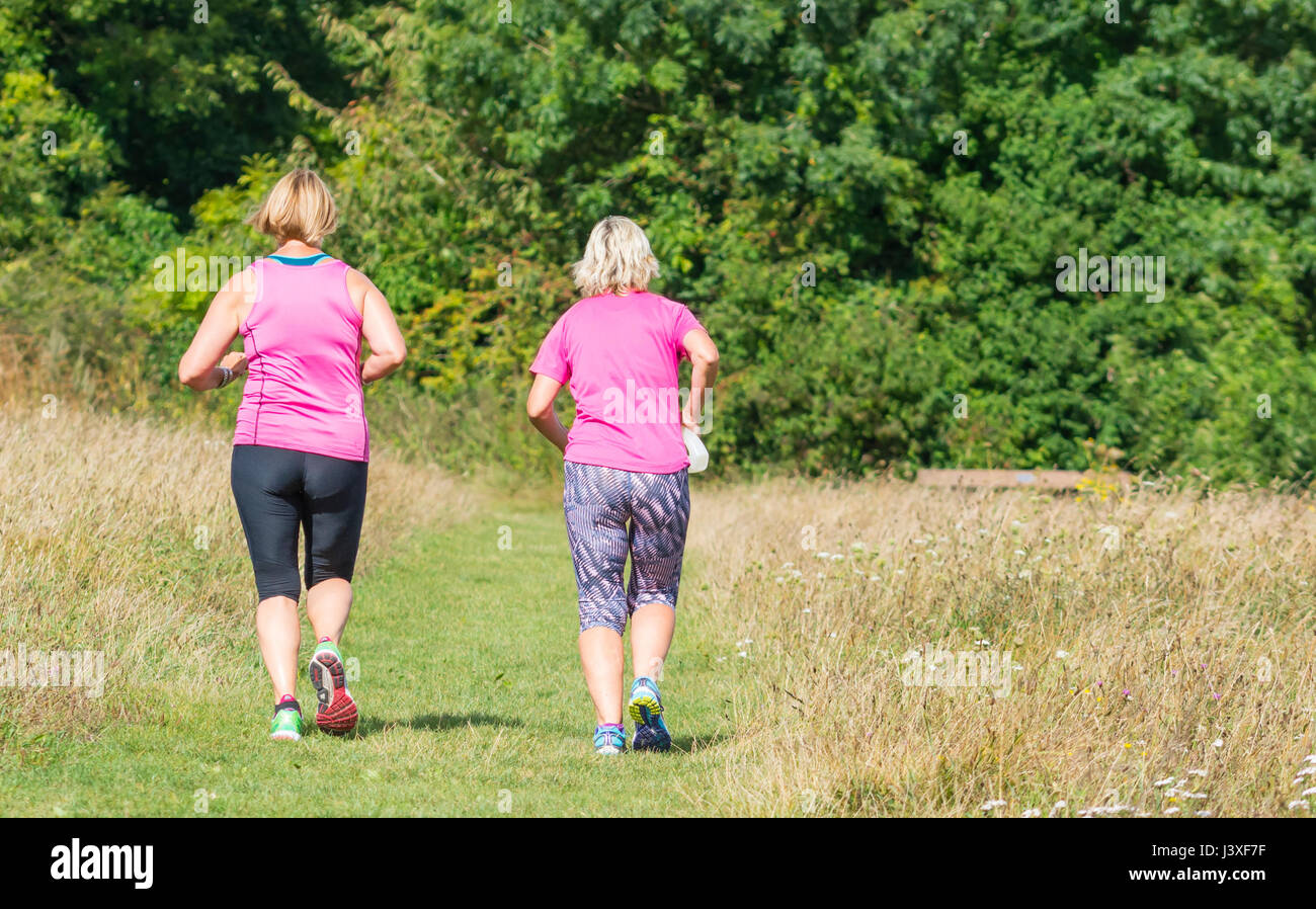 Coppia di donne praticanti di jogging jogging attraverso i campi nella campagna britannica. Esercizio di concetto. Mantenere la misura del concetto. Foto Stock