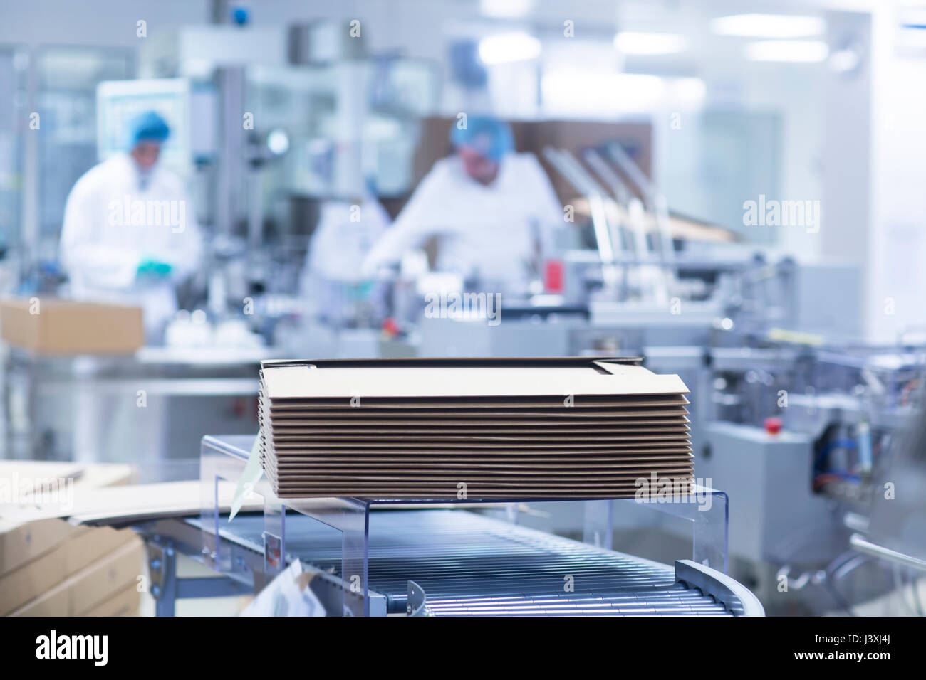 I lavoratori sulla linea di produzione in impianto farmaceutico, scatole di cartone impilate in primo piano Foto Stock