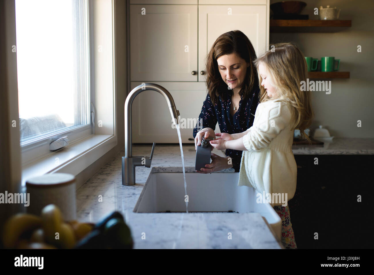 Donna aiutando la figlia di lavare le mani al lavello da cucina Foto Stock