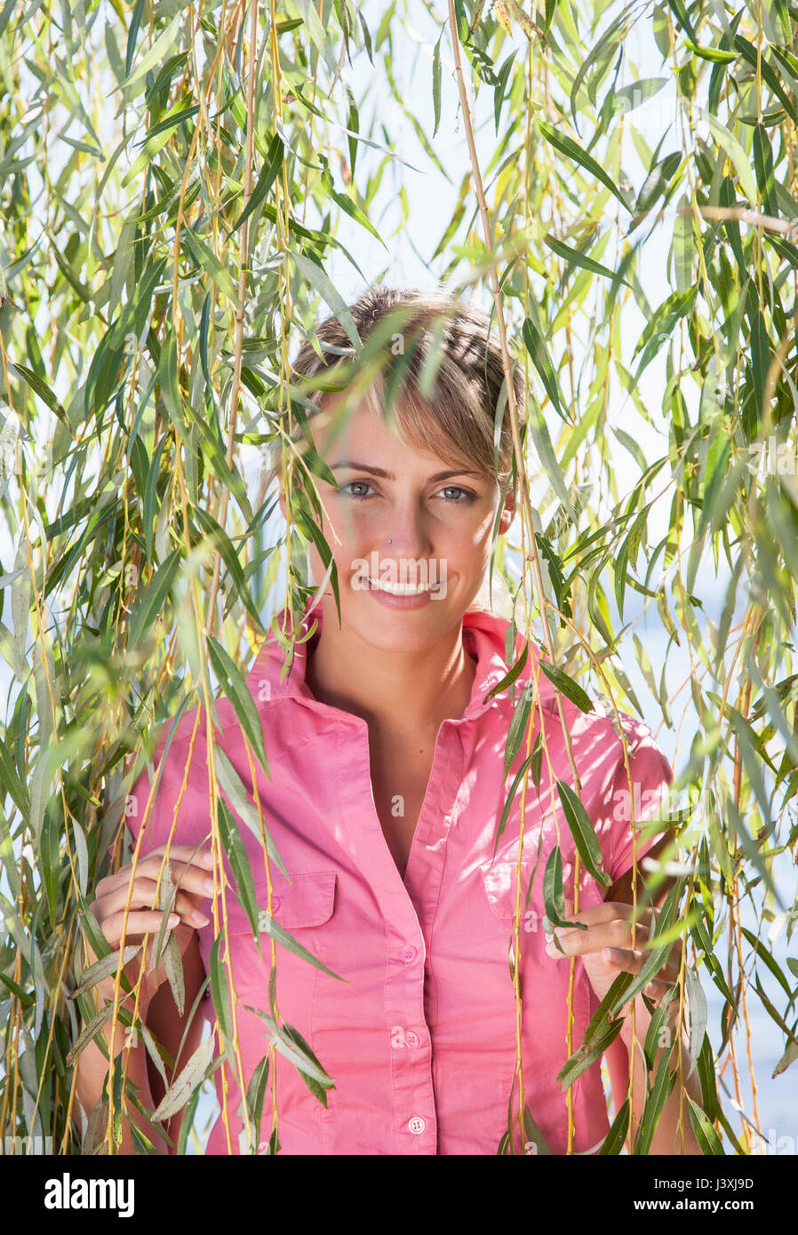 Ritratto di donna sorridente tra salice piangente rami, Lago Maggiore, Italia Foto Stock
