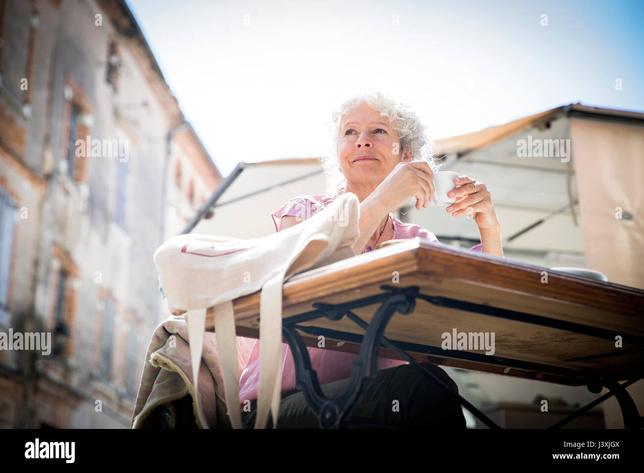 Donna al cafe' sul marciapiede che guarda lontano, Bruniquel, Francia Foto Stock
