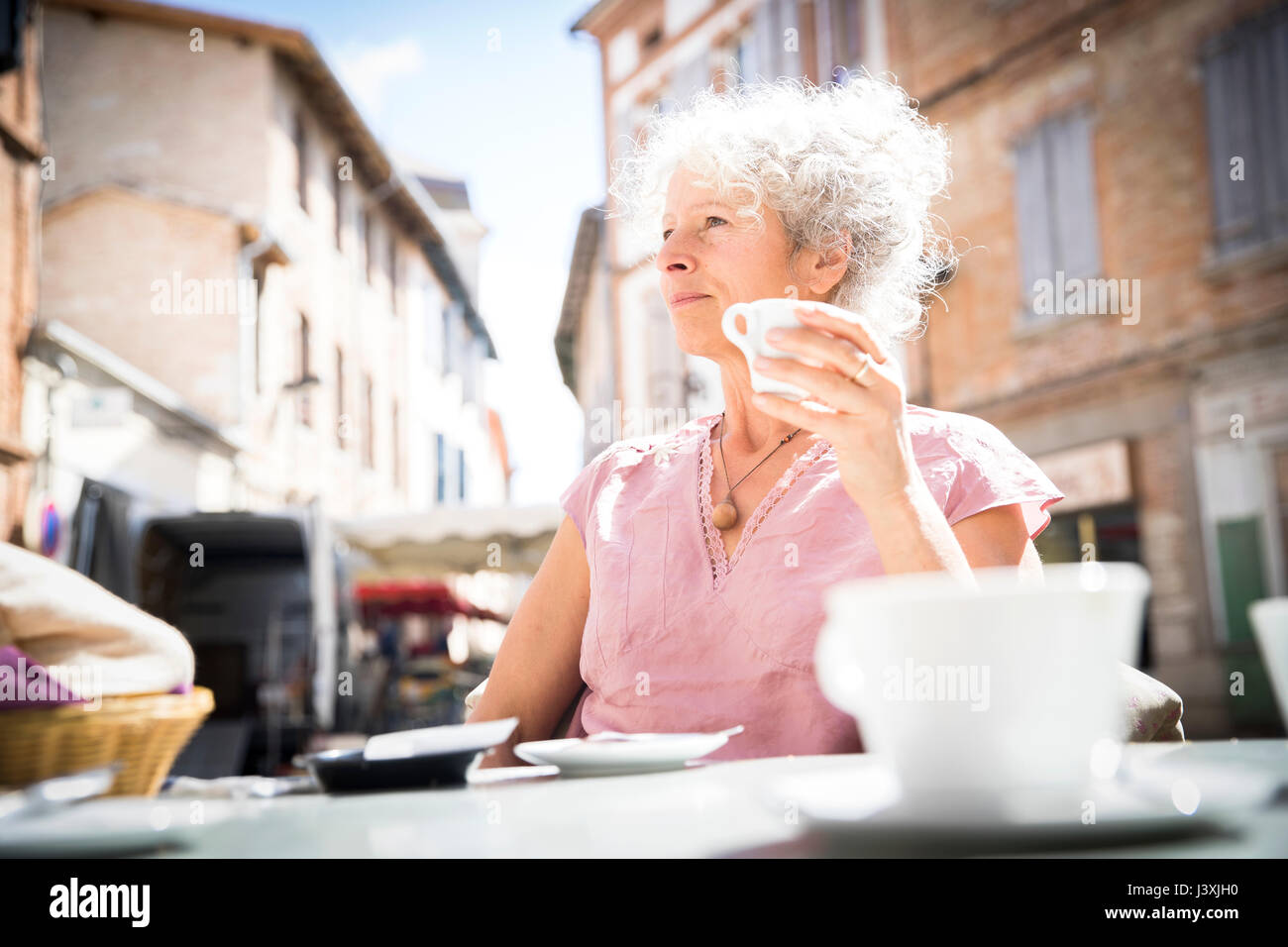 Donna al cafe' sul marciapiede che guarda lontano, Bruniquel, Francia Foto Stock
