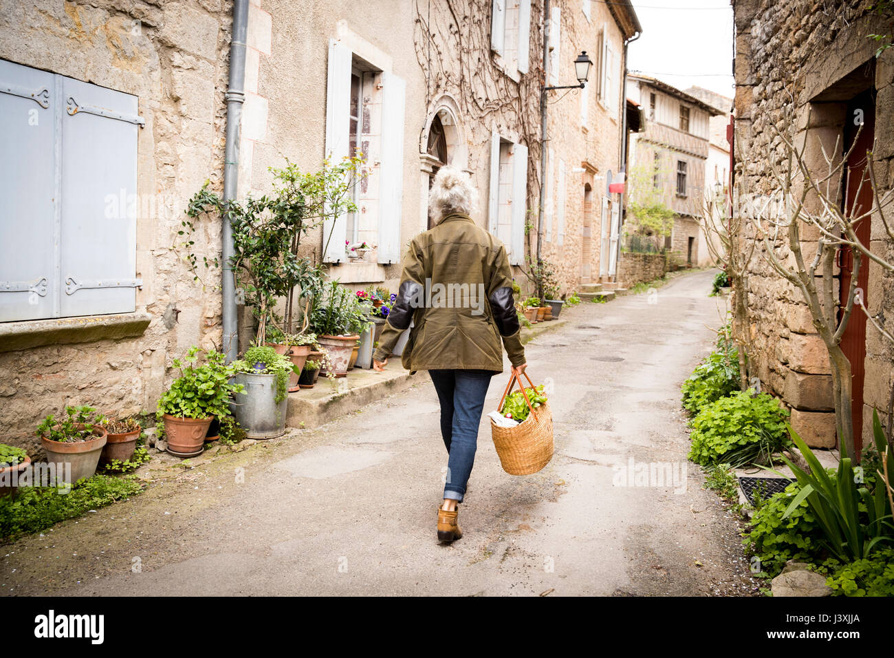 Vista posteriore della donna a piedi nella stretta strada rurale, Bruniquel, Francia Foto Stock