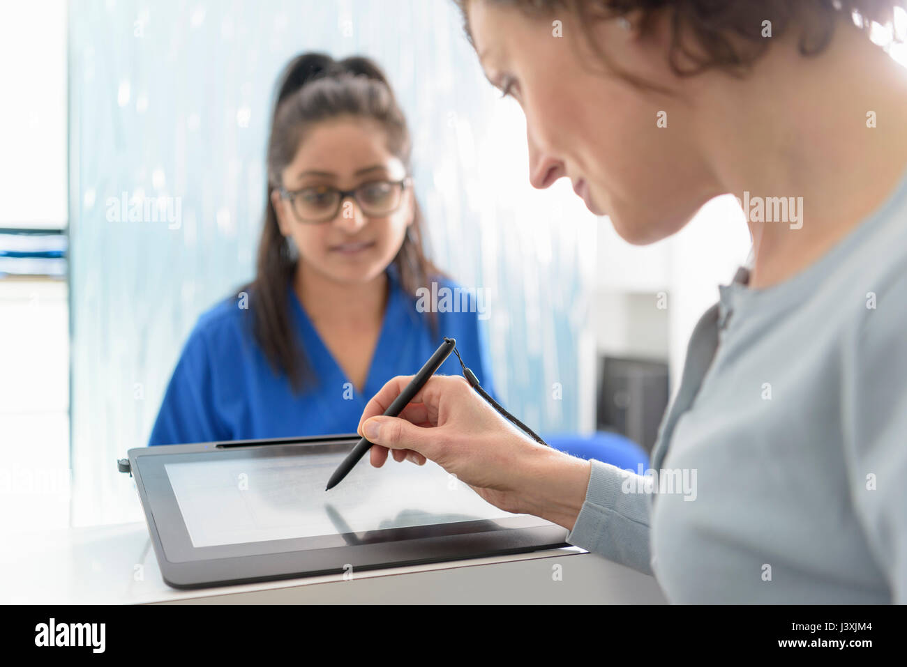 Receptionist dentale assistere il paziente compila il modulo sulla tavoletta digitale in chirurgia dentale Foto Stock
