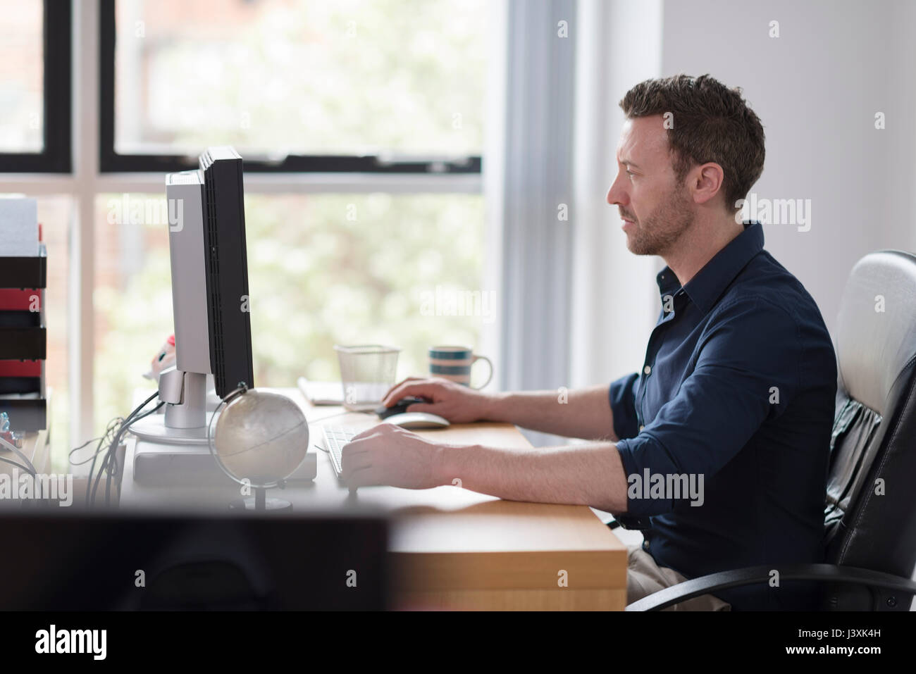 Uomo che lavora al computer sulla scrivania in ufficio Foto Stock