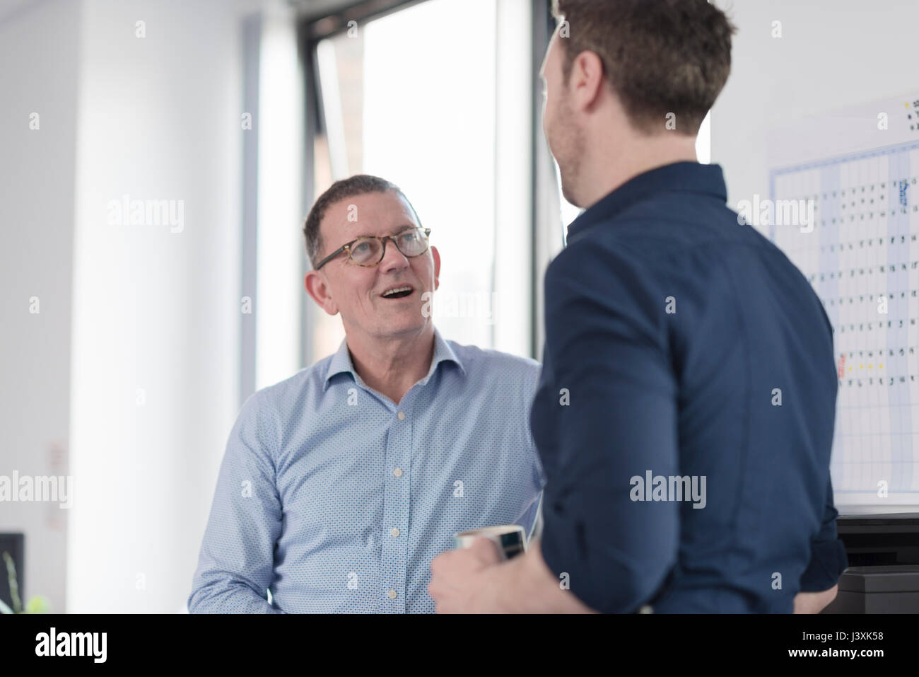 Colleghi di sesso maschile parlando dalla macchina copiatrice Foto Stock