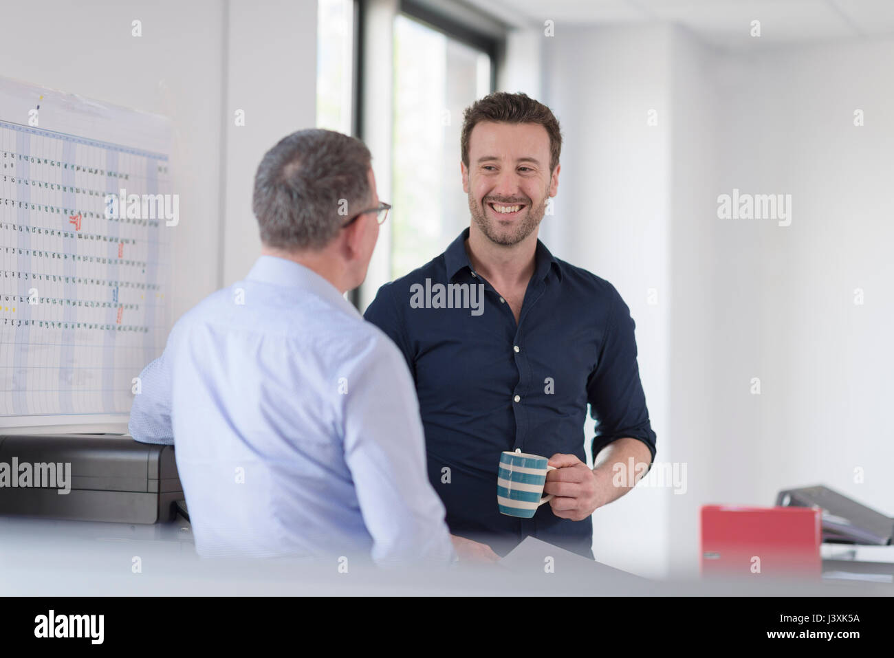 Colleghi di sesso maschile parlando dalla macchina copiatrice Foto Stock