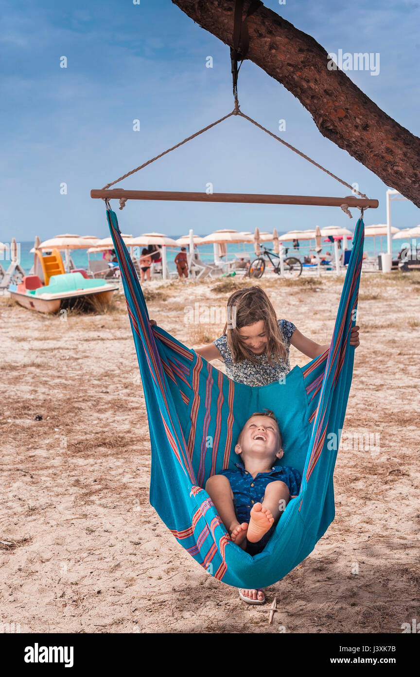 Ragazza spingendo fratello in amaca sulla spiaggia del Poetto di Cagliari, Italia Foto Stock