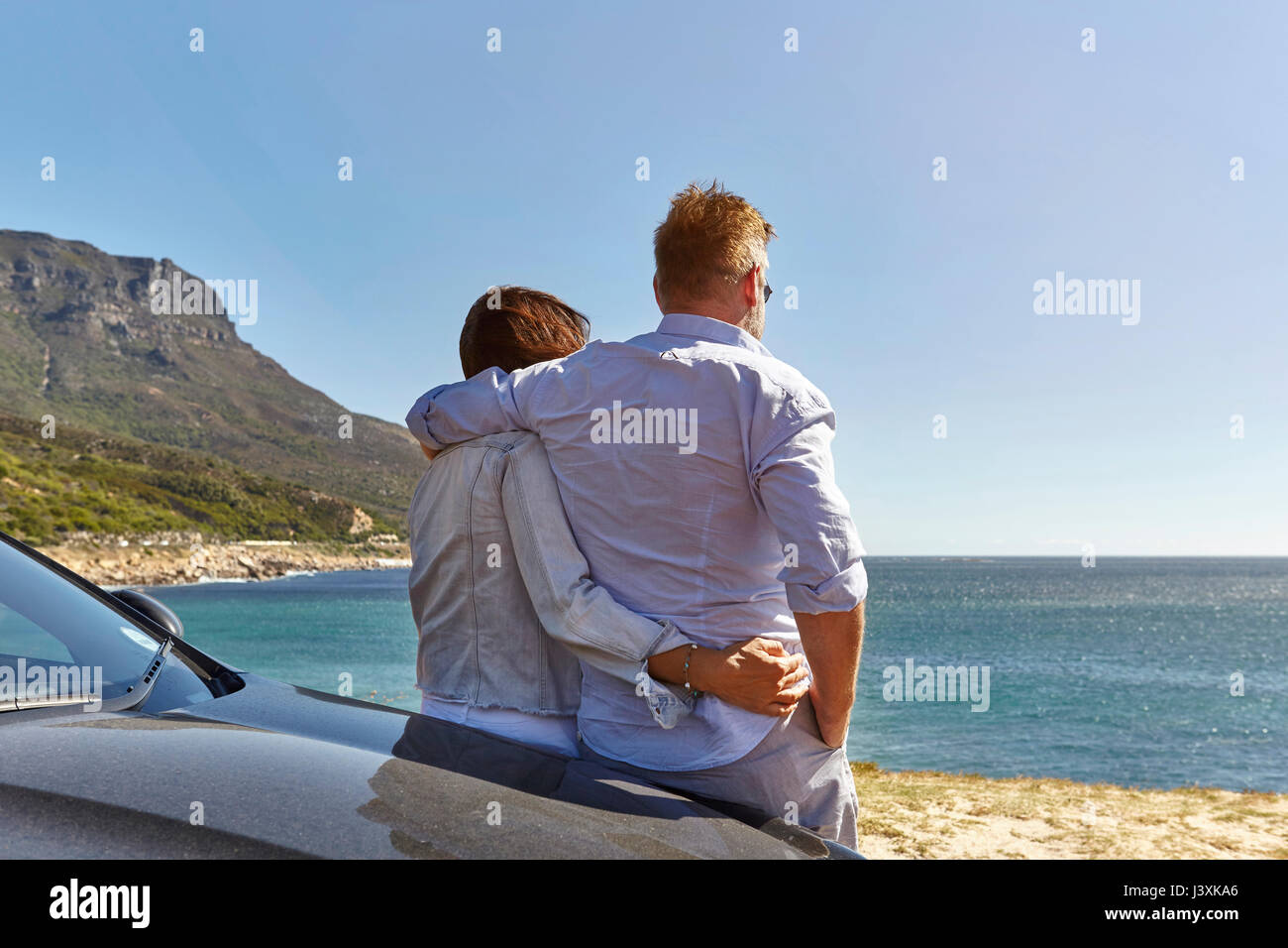 Giovane appoggiata sul cofano auto, guardando a vista costiera, vista posteriore, Città del Capo Foto Stock