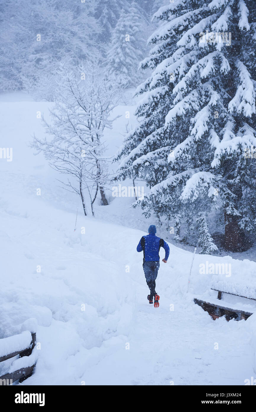 Vista posteriore dei maschi di runner acceso sulla via nella neve profonda, Gstaad, Svizzera Foto Stock