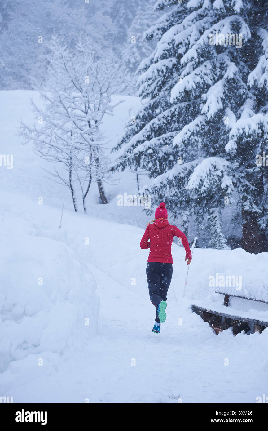 Vista posteriore del femminile in esecuzione sulla via nella neve profonda, Gstaad, Svizzera Foto Stock