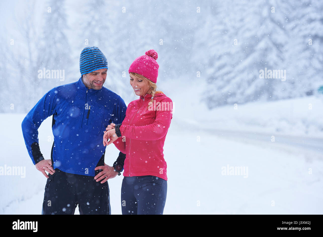 Maschi e femmine di guide di scorrimento Controllo smartwatch su neve profonda traccia, Gstaad, Svizzera Foto Stock