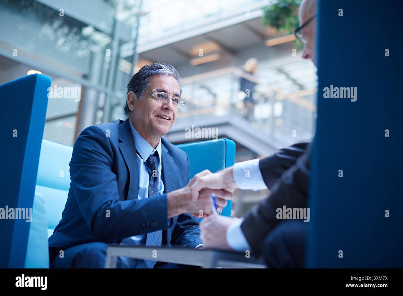 Due imprenditori stringono le mani in office atrium Foto Stock
