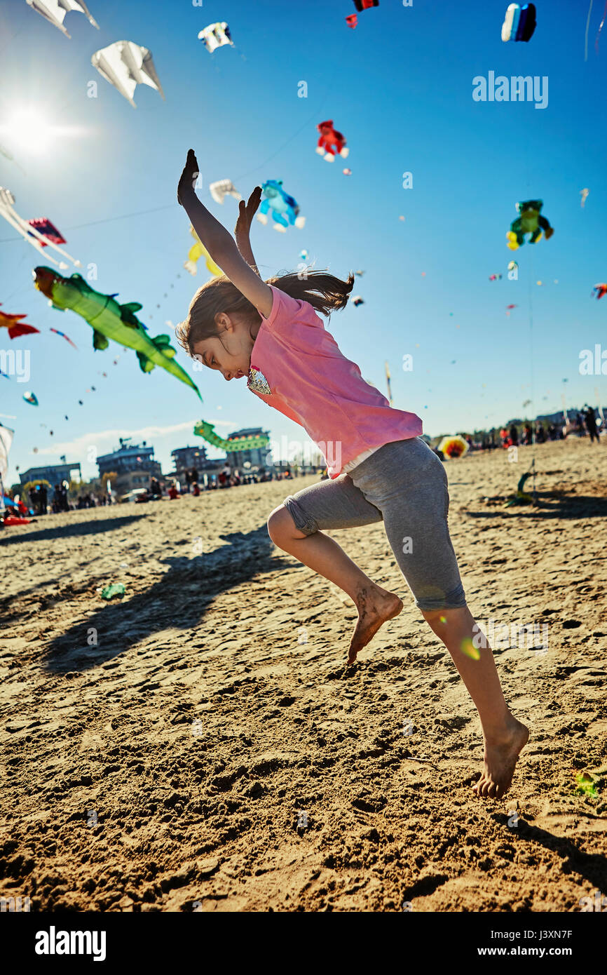 Ragazza giovane facendo appoggiate sulla spiaggia, aquiloni volare nel cielo dietro di lei, Rimini, Italia Foto Stock