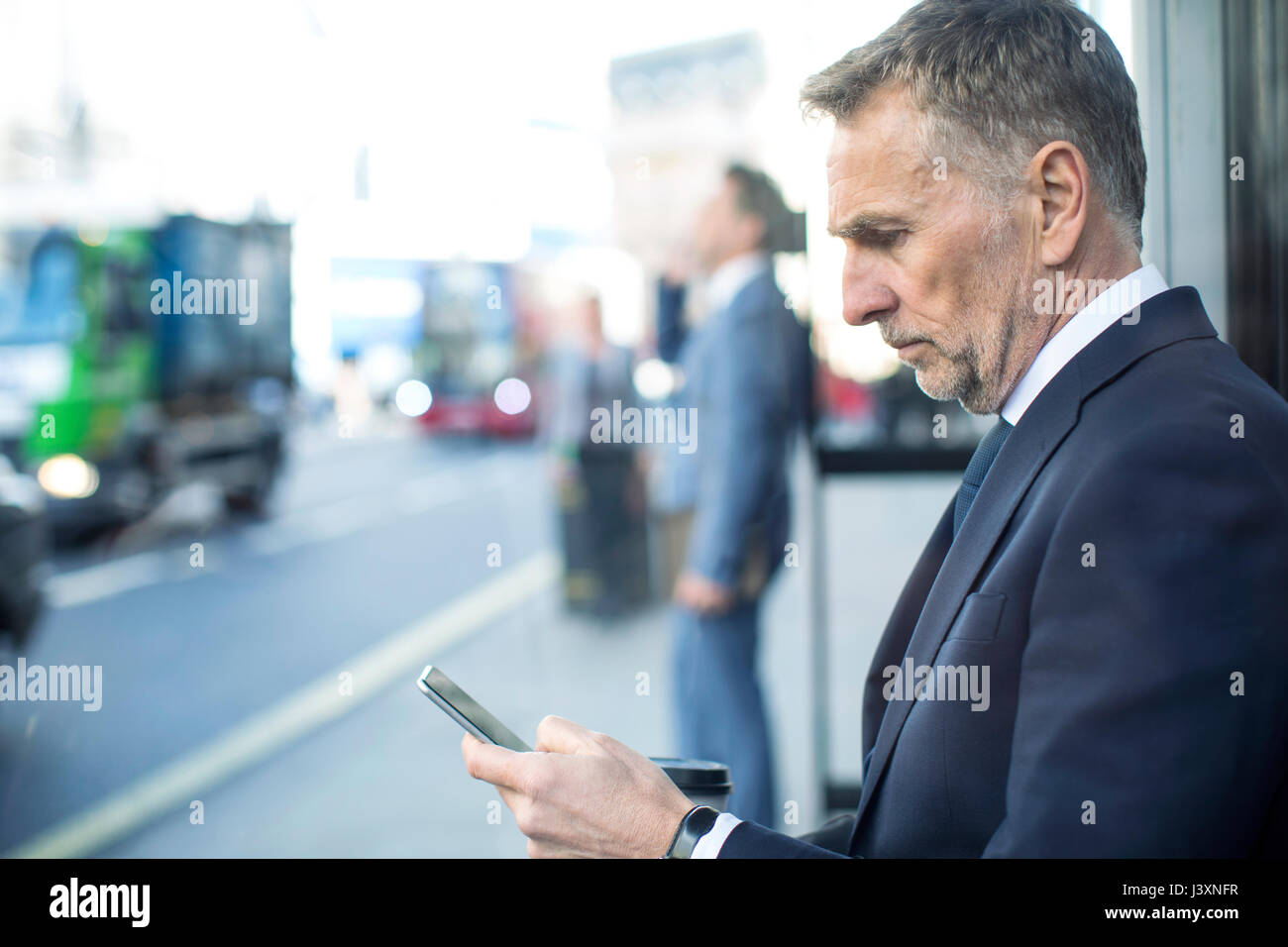Imprenditore in attesa presso la fermata utilizza lo smartphone, London, Regno Unito Foto Stock